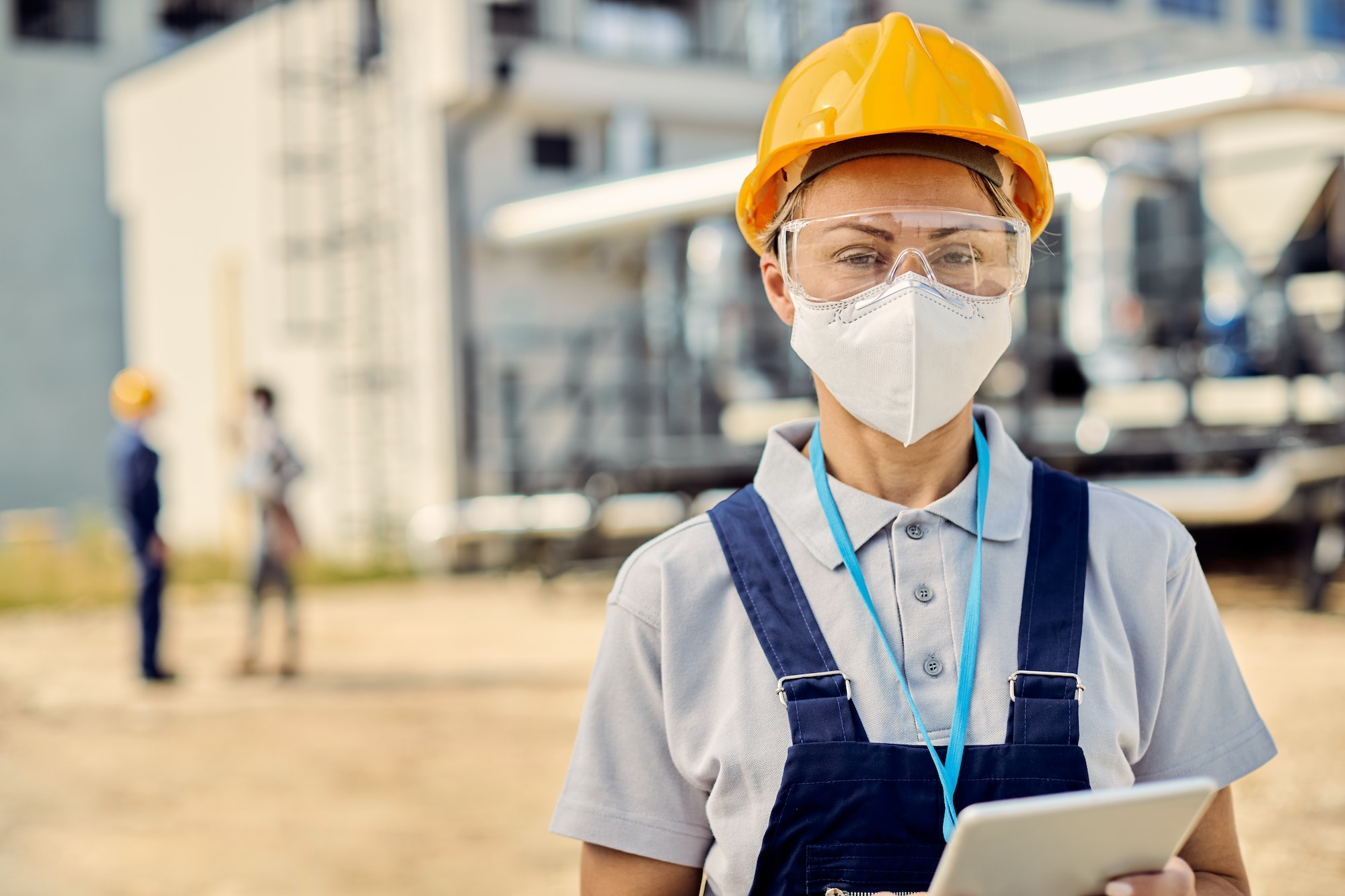 Female building contractor with digital tablet wearing face mask at construction site.