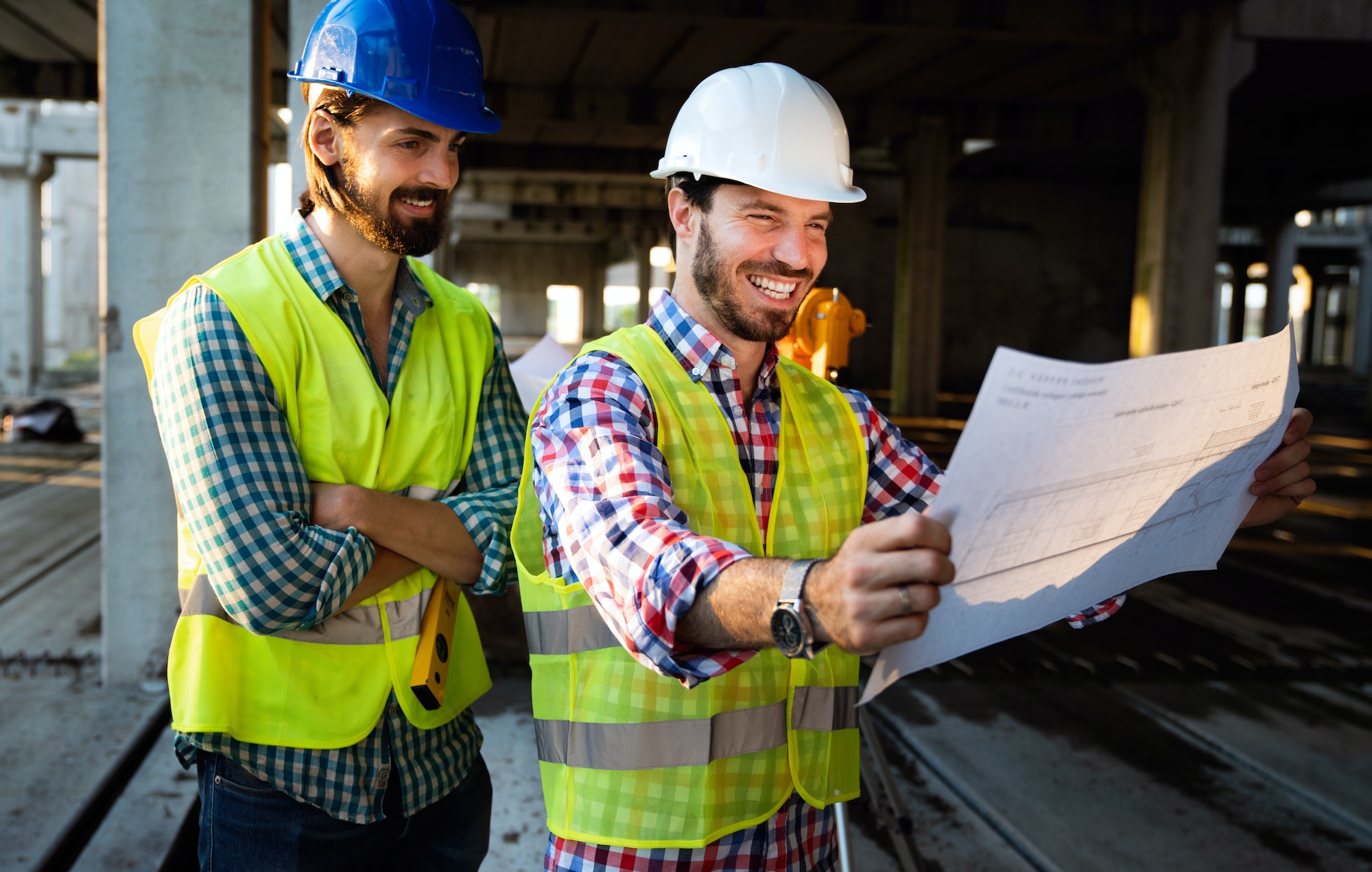 Two satisfied engineers talking at building site with construction structure in background